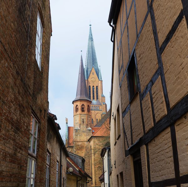 Der Kirchturm des St.-Petri-Doms aus einer Gasse heraus zwischen zwei Häusern fotografiert.