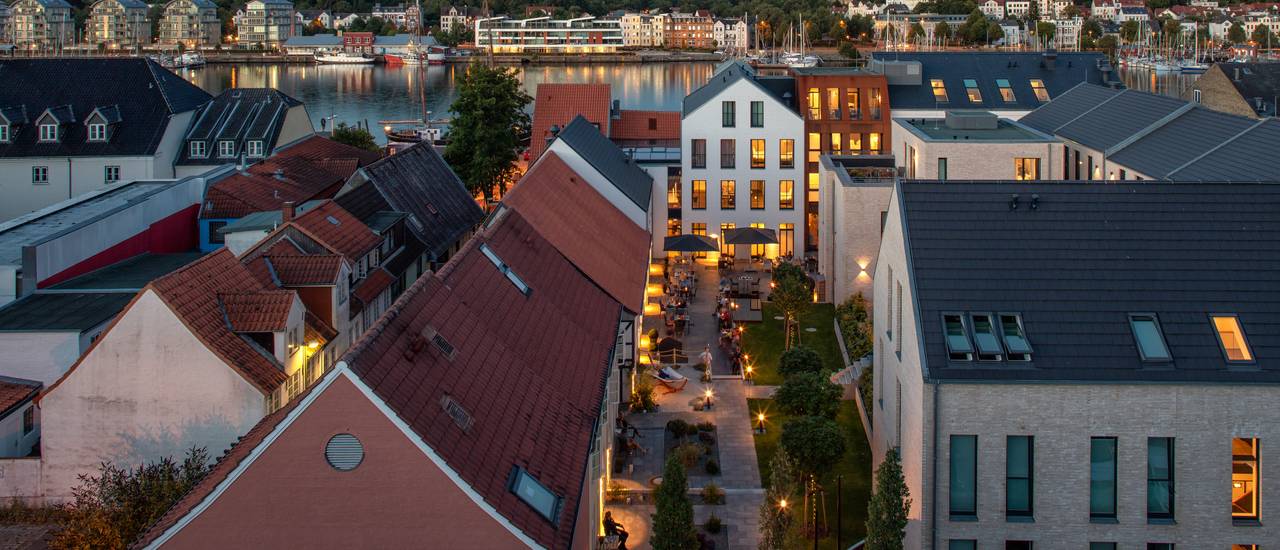 Aerial view from the west in the illuminated courtyard garden of the Hotel Hafen Flensburg just before dawn.