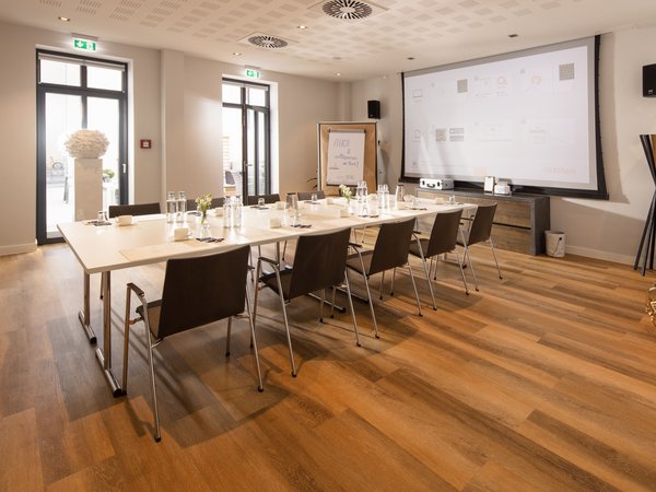Mødet og arrangementet Herrenstall 1 og 2 i Hotel Hafen Flensburg med et overdækket bord, der peger på siden af ​​skærmen.